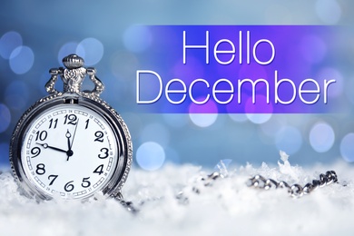 Image of Greeting card with text Hello December. Pocket watch on snow against blurred Christmas lights