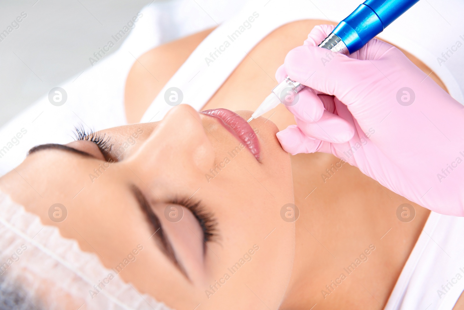 Photo of Young woman getting permanent makeup on lips in beautician salon, closeup