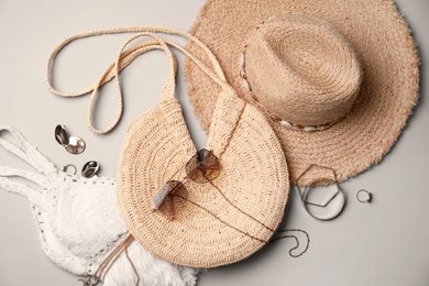 Stylish straw bag and summer accessories on grey background, flat lay