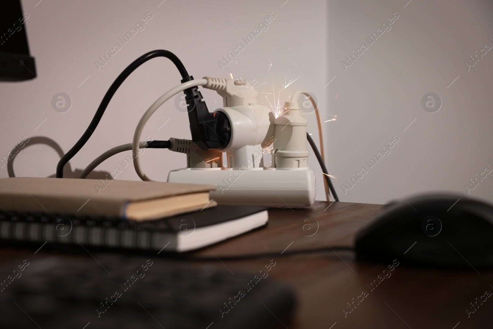 Photo of Inflamed plug in power strip indoors on wooden table. Electrical short circuit