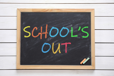 Image of Chalkboard with text SCHOOL'S OUT on white wooden background, top view