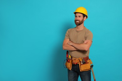Photo of Professional builder in hard hat with tool belt on light blue background, space for text