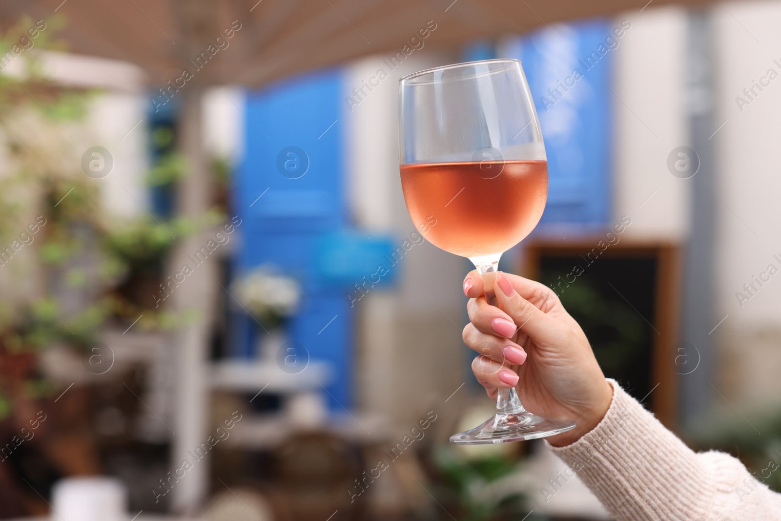 Photo of Woman holding glass of rose wine outdoors, closeup. Space for text