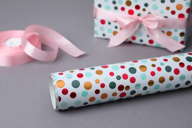 Photo of Roll of wrapping paper, gift box and pink ribbon on grey background, closeup