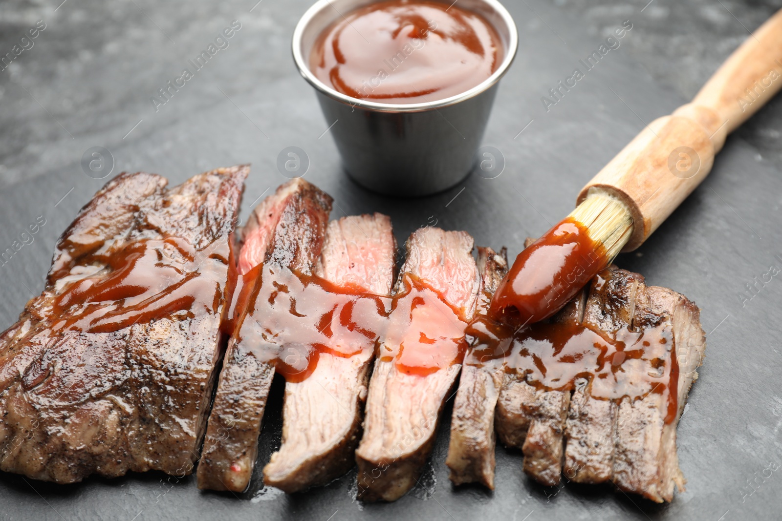 Photo of Pieces of delicious roasted beef meat with sauce on black table, closeup