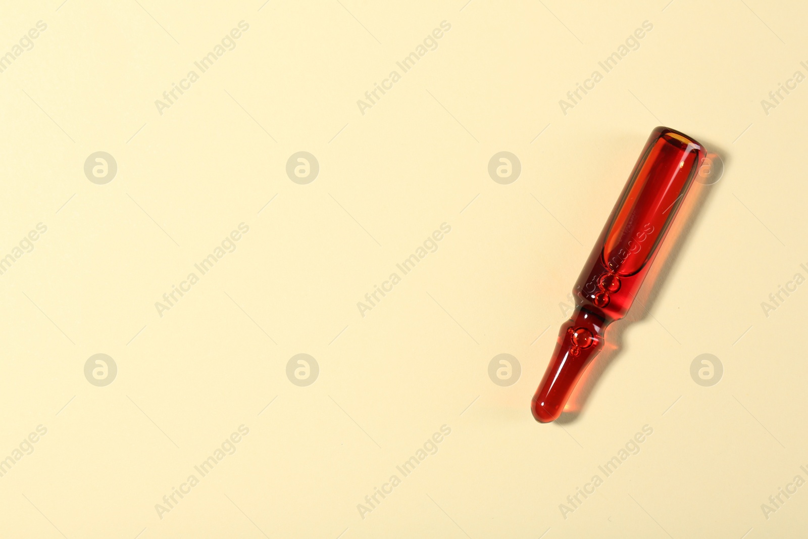 Photo of Glass ampoule with liquid on beige background, top view. Space for text