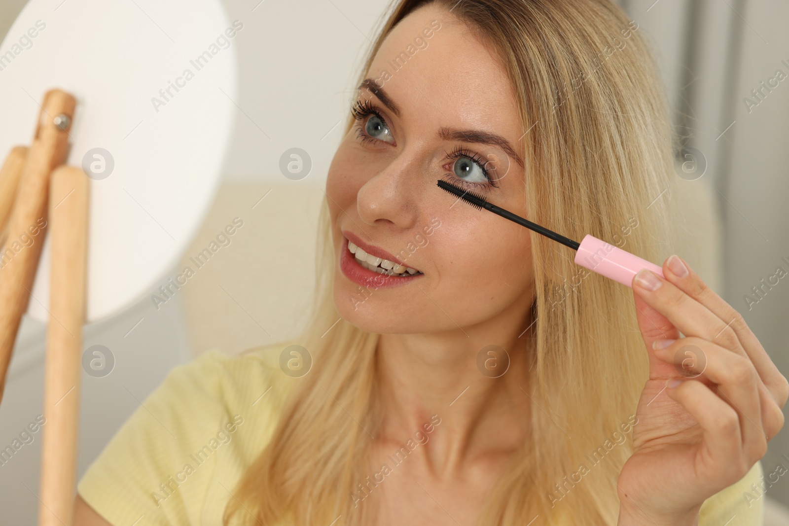 Photo of Beautiful woman with mirror applying mascara indoors, closeup
