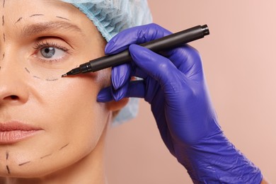 Photo of Doctor with marker preparing patient for cosmetic surgery operation on light brown background, closeup