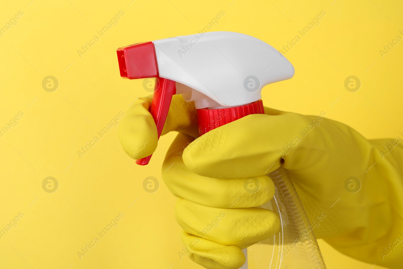 Photo of Woman holding plastic spray bottle on yellow background, closeup