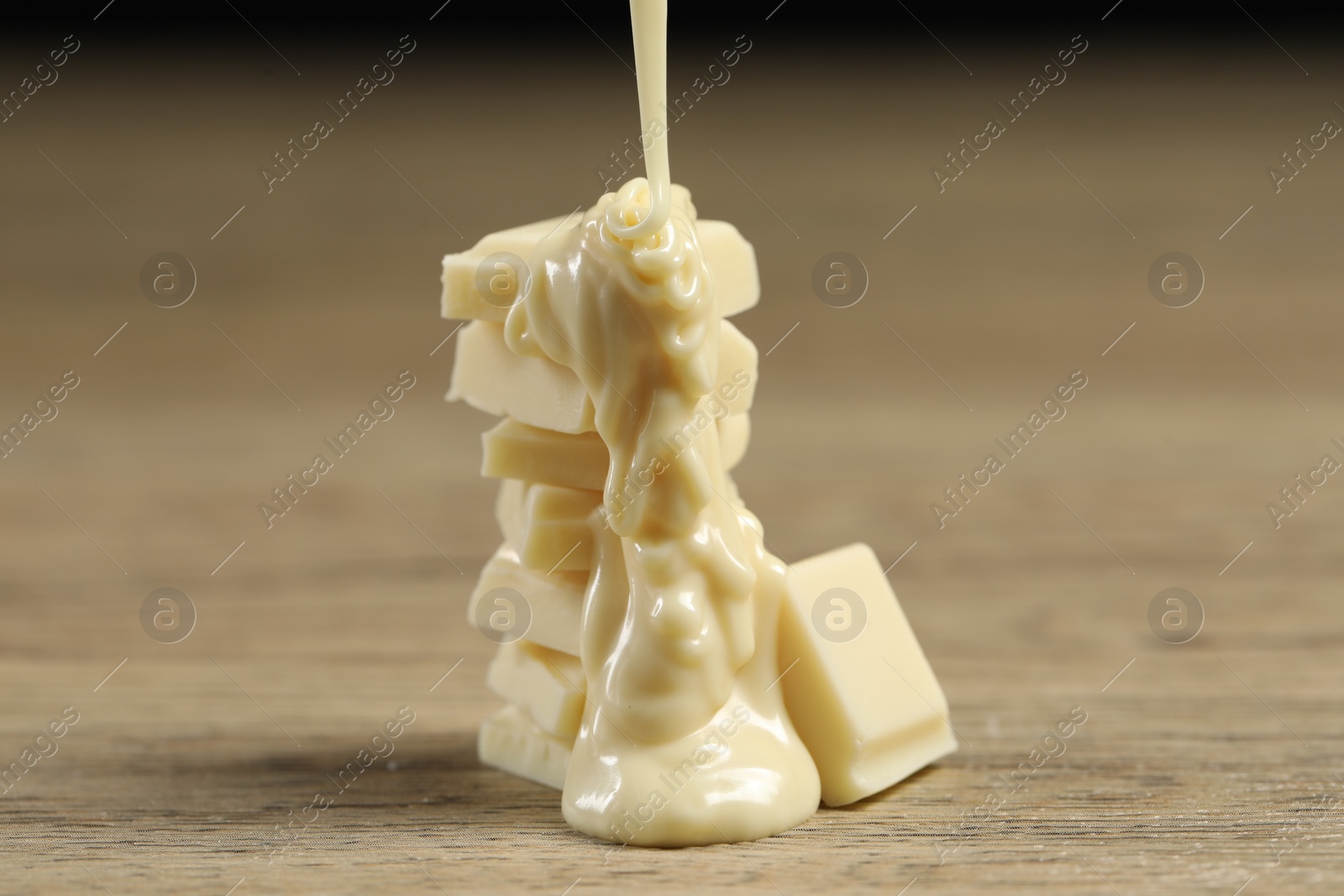 Photo of Pouring tasty white chocolate paste onto pieces on wooden table, closeup