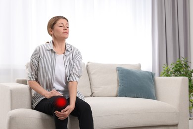 Image of Woman suffering from pain in knee on sofa at home. Space for text