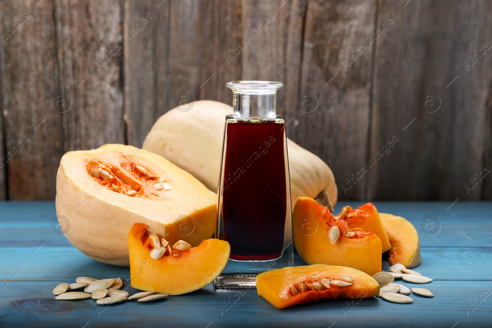 Photo of Fresh pumpkin seed oil in glass bottle on blue wooden table