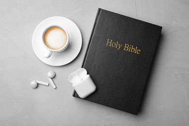 Photo of Bible, cup of coffee and earphones on light grey background, flat lay. Religious audiobook