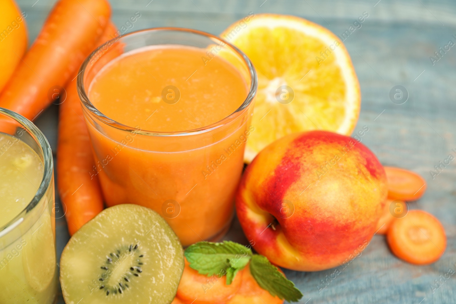 Photo of Glasses of delicious juices and fresh ingredients on light blue table, closeup