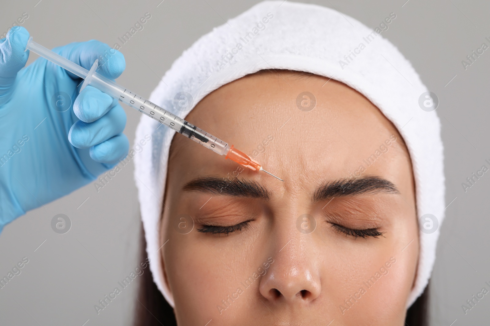 Photo of Doctor giving facial injection to young woman on light grey background, closeup. Cosmetic surgery