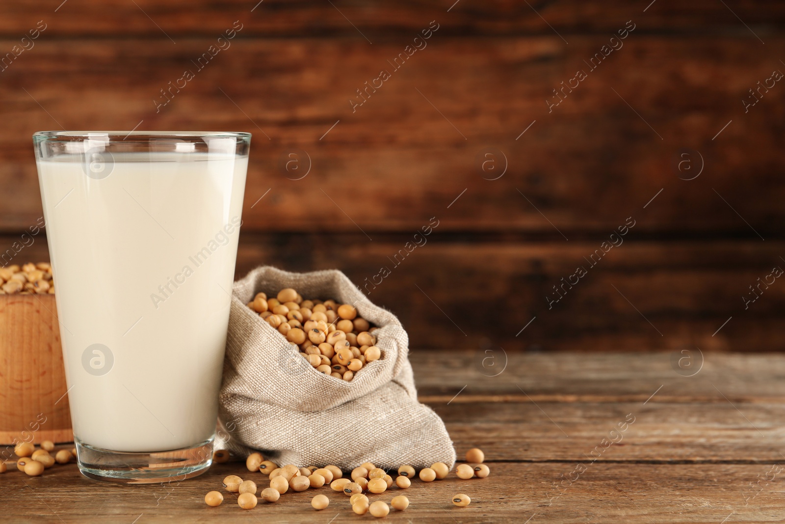 Photo of Glass with fresh soy milk and grains on wooden table. Space for text