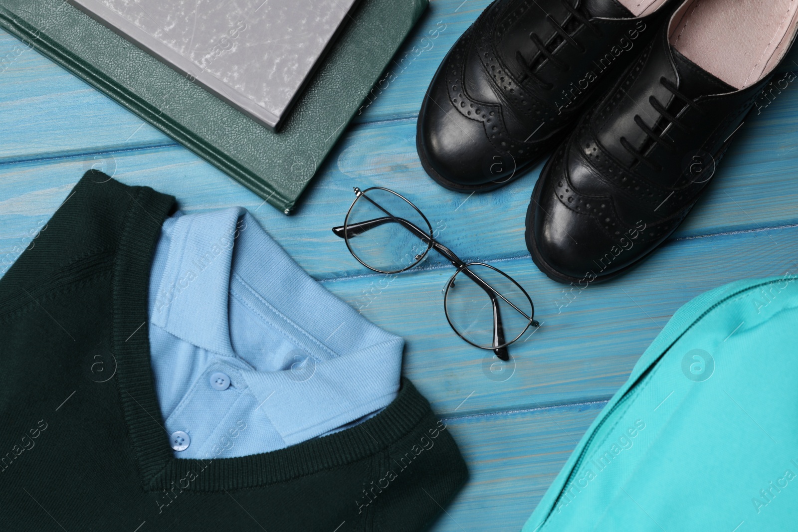 Photo of Stylish school uniform for boy, glasses, books and backpack on light blue wooden background, flat lay