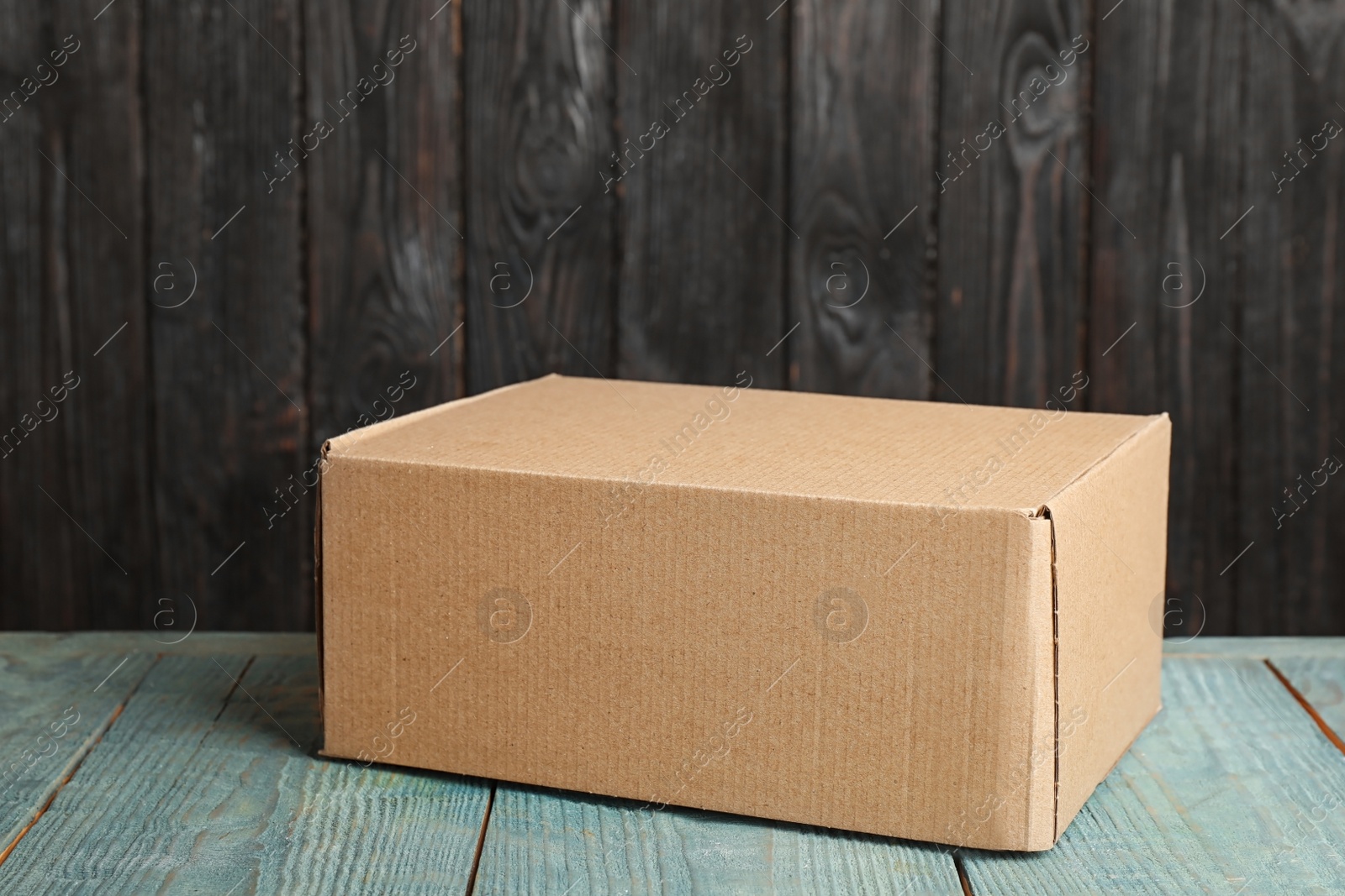 Photo of Cardboard box on light blue wooden table against dark background