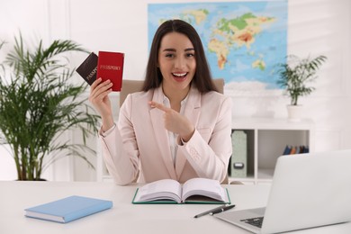 Happy manager holding passports at desk in travel agency