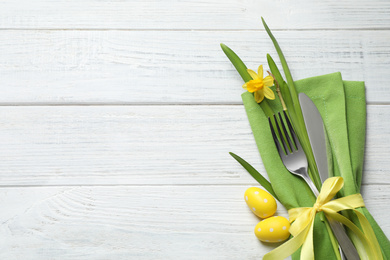Photo of Cutlery set and beautiful narcissus on white wooden table, top view with space for text. Easter celebration