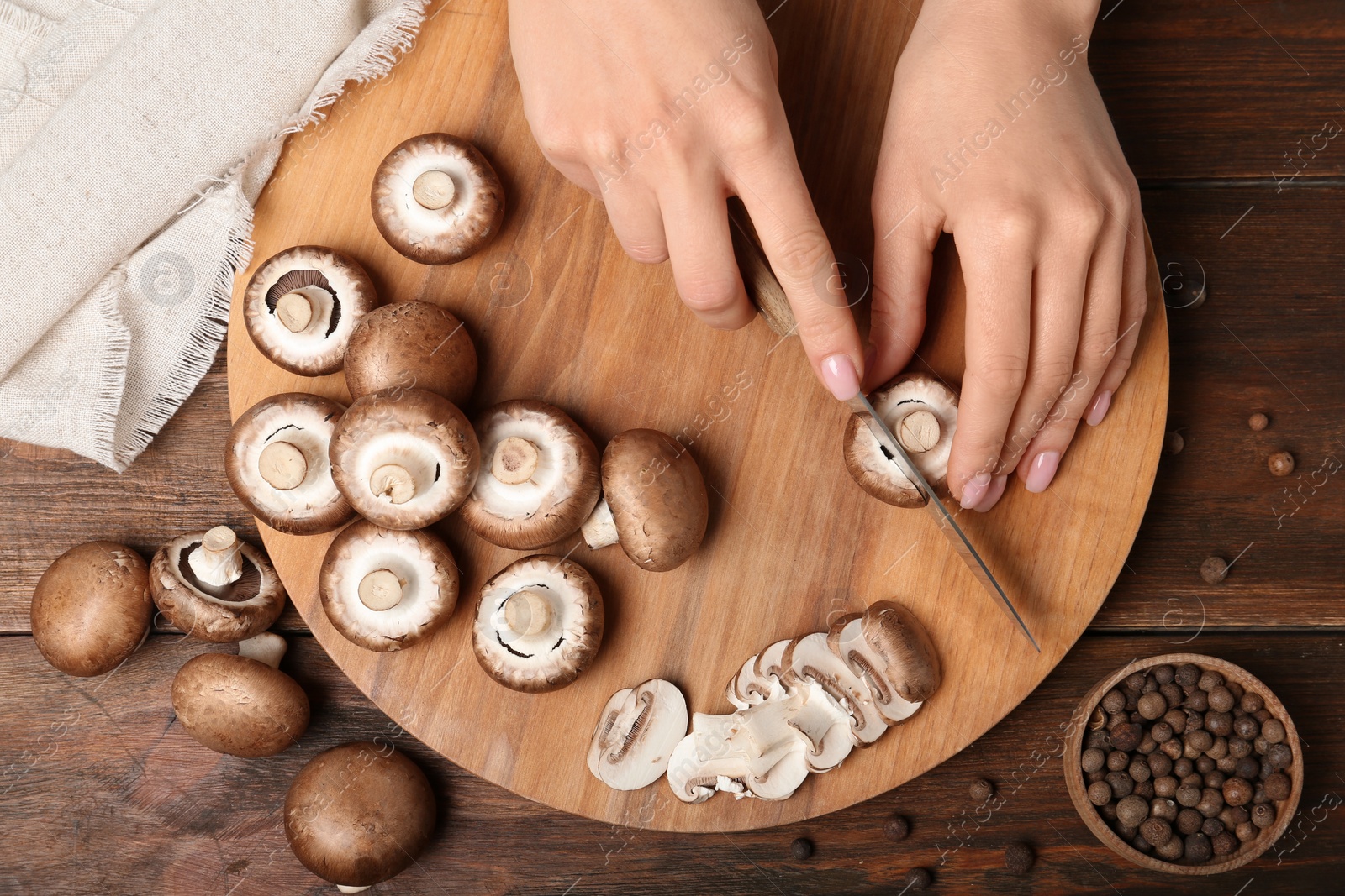 Photo of Young woman cutting fresh champignon mushrooms on wooden board, top view