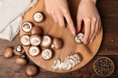 Young woman cutting fresh champignon mushrooms on wooden board, top view