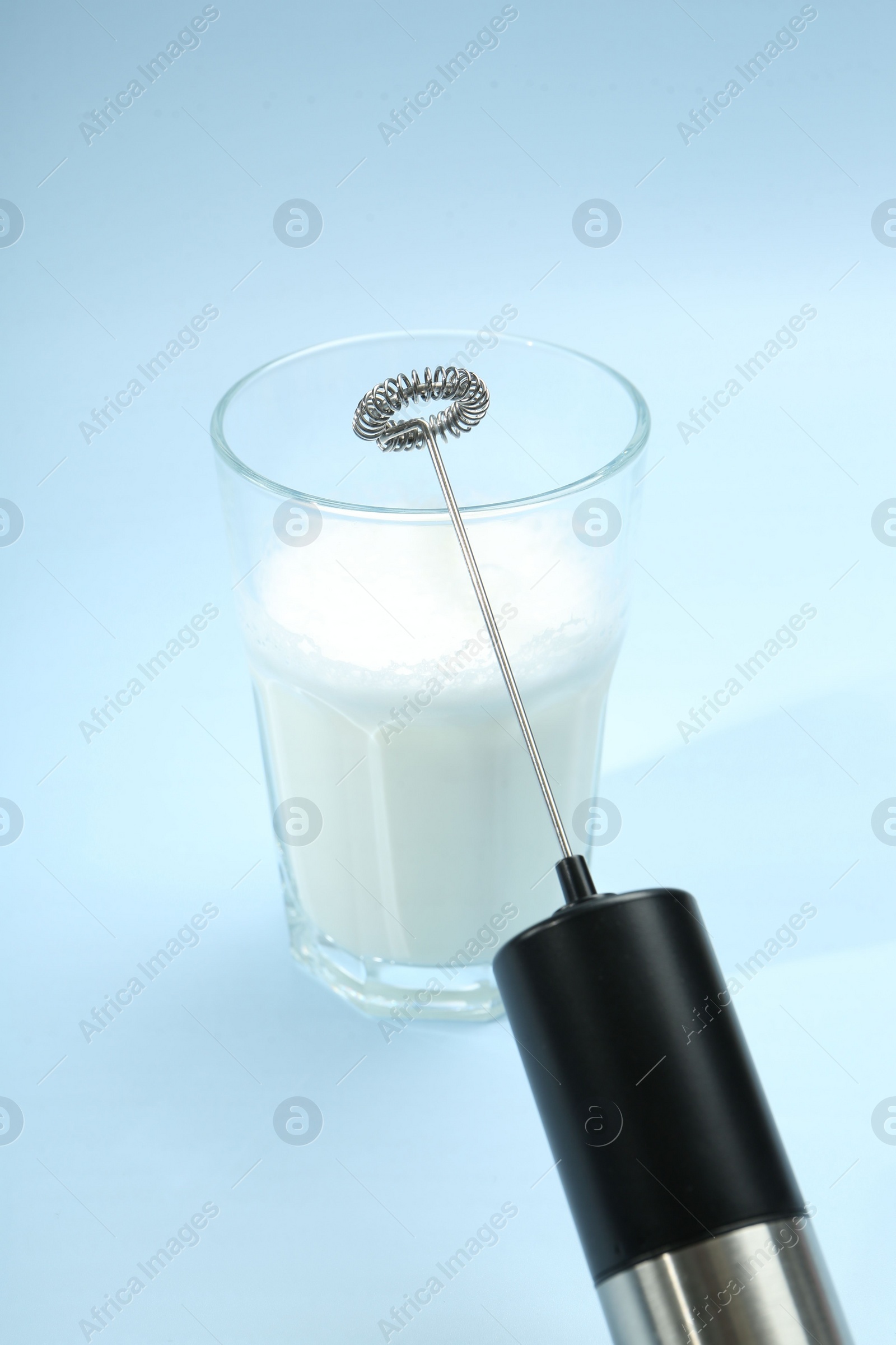 Photo of Mini mixer (milk frother) and whipped milk in glass on light blue background