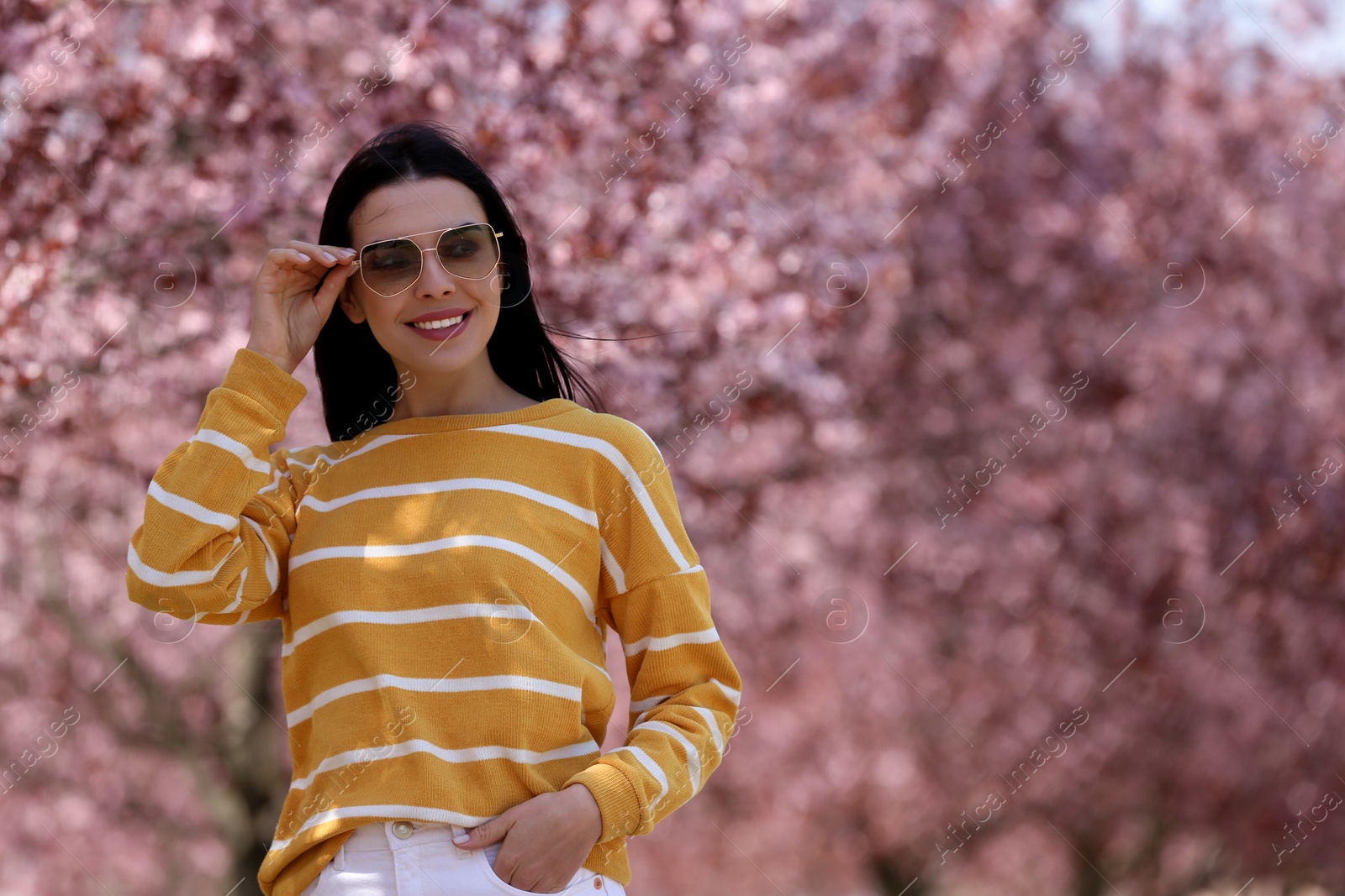 Photo of Pretty young woman with sunglasses near beautiful blossoming trees outdoors. Stylish spring look