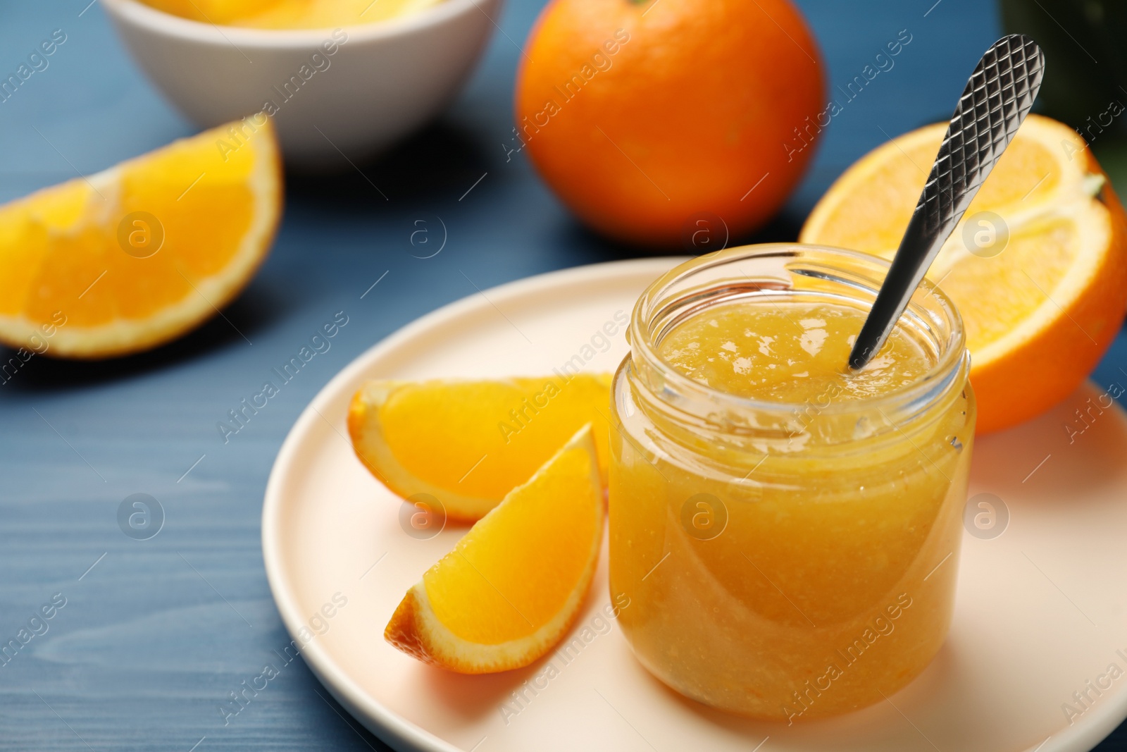 Photo of Delicious orange marmalade and fruit slices on blue wooden table