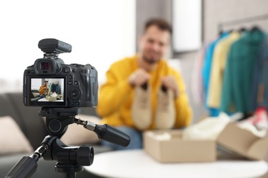 Photo of Fashion blogger showing shoes while recording video at home, focus on camera