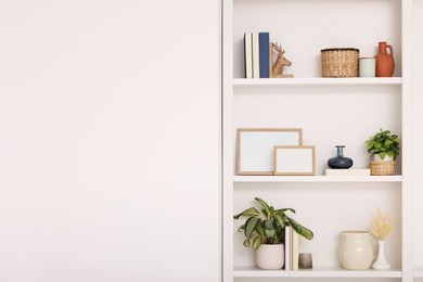 Photo of Interior design. Shelves with stylish accessories, potted plants and frames near white wall. Space for text