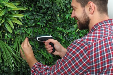 Photo of Man with screwdriver installing green artificial plant wall panel indoors