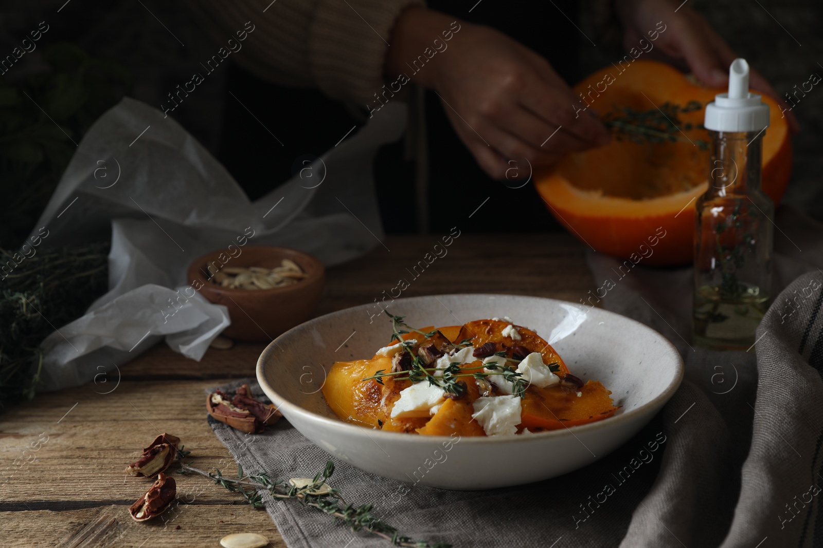 Photo of Baked pumpkin slices served with cheese, thyme and pecans on wooden table, selective focus. Space for text