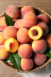 Cut and whole fresh ripe peaches with green leaves in basket on wooden table, top view