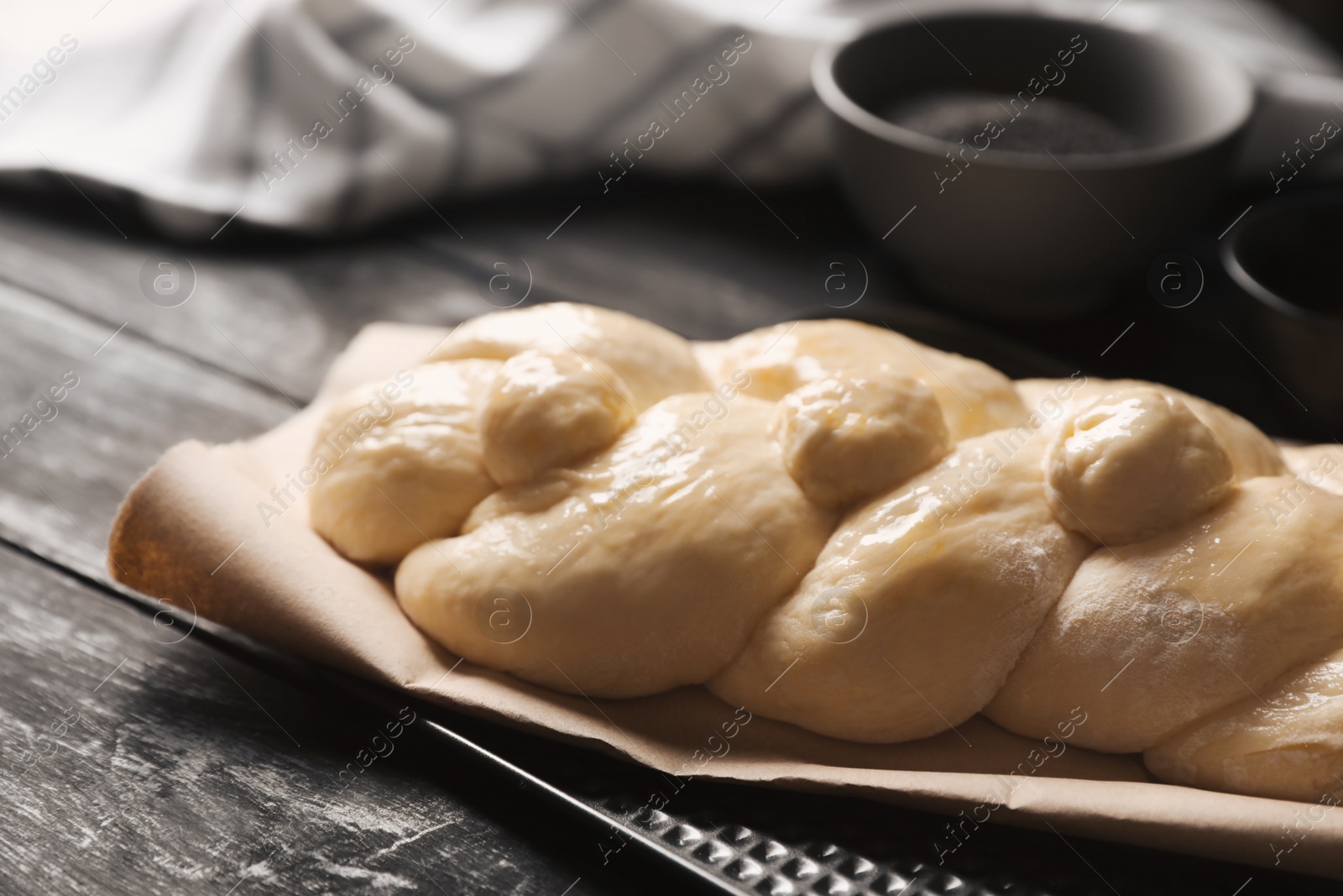 Photo of Raw braided bread and ingredients on black wooden table, closeup. Traditional Shabbat challah