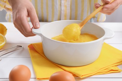 Photo of Woman cooking lemon curd at white wooden table, closeup