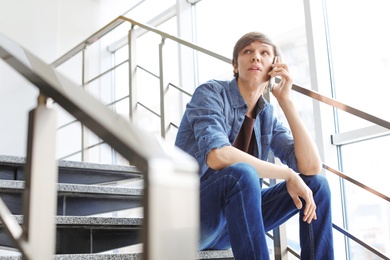 Photo of Portrait of confident young man with mobile phone on stairs