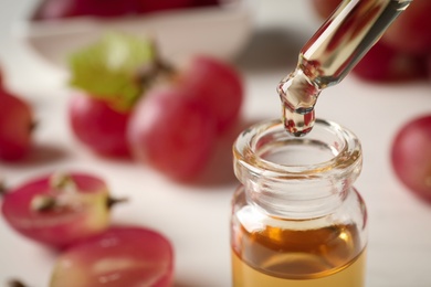 Photo of Dripping natural grape seed oil from pipette into glass bottle on table, closeup with space for text. Organic cosmetic