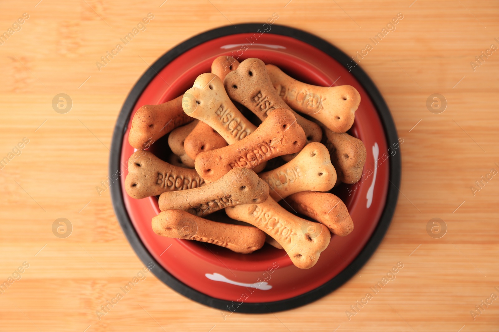 Photo of Bone shaped dog cookies in feeding bowl on wooden table, top view