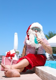 Photo of Authentic Santa Claus with cocktail and gift in bag near pool at resort