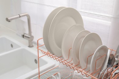 Photo of Drying rack with clean dishes near sink in kitchen, closeup
