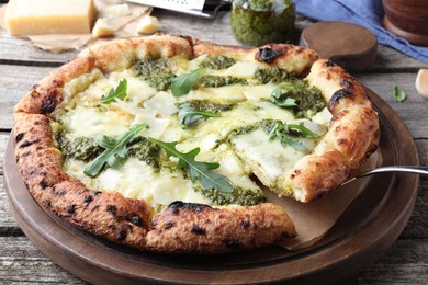 Taking slice of delicious pizza with pesto, cheese and arugula on wooden table, closeup