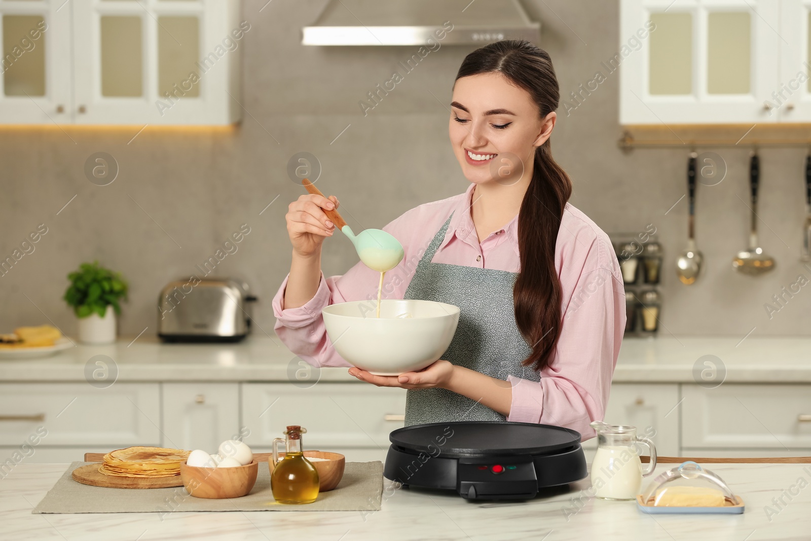 Photo of Happy woman with dough for crepes at white marble table in kitchen