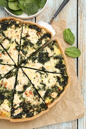 Delicious homemade quiche and fresh spinach leaves on table, flat lay