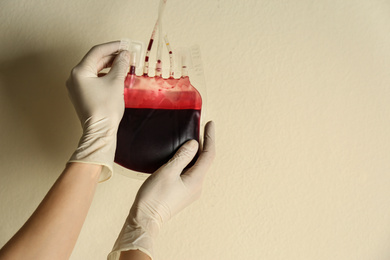 Photo of Woman holding blood for transfusion on beige background, closeup with space for text. Donation concept