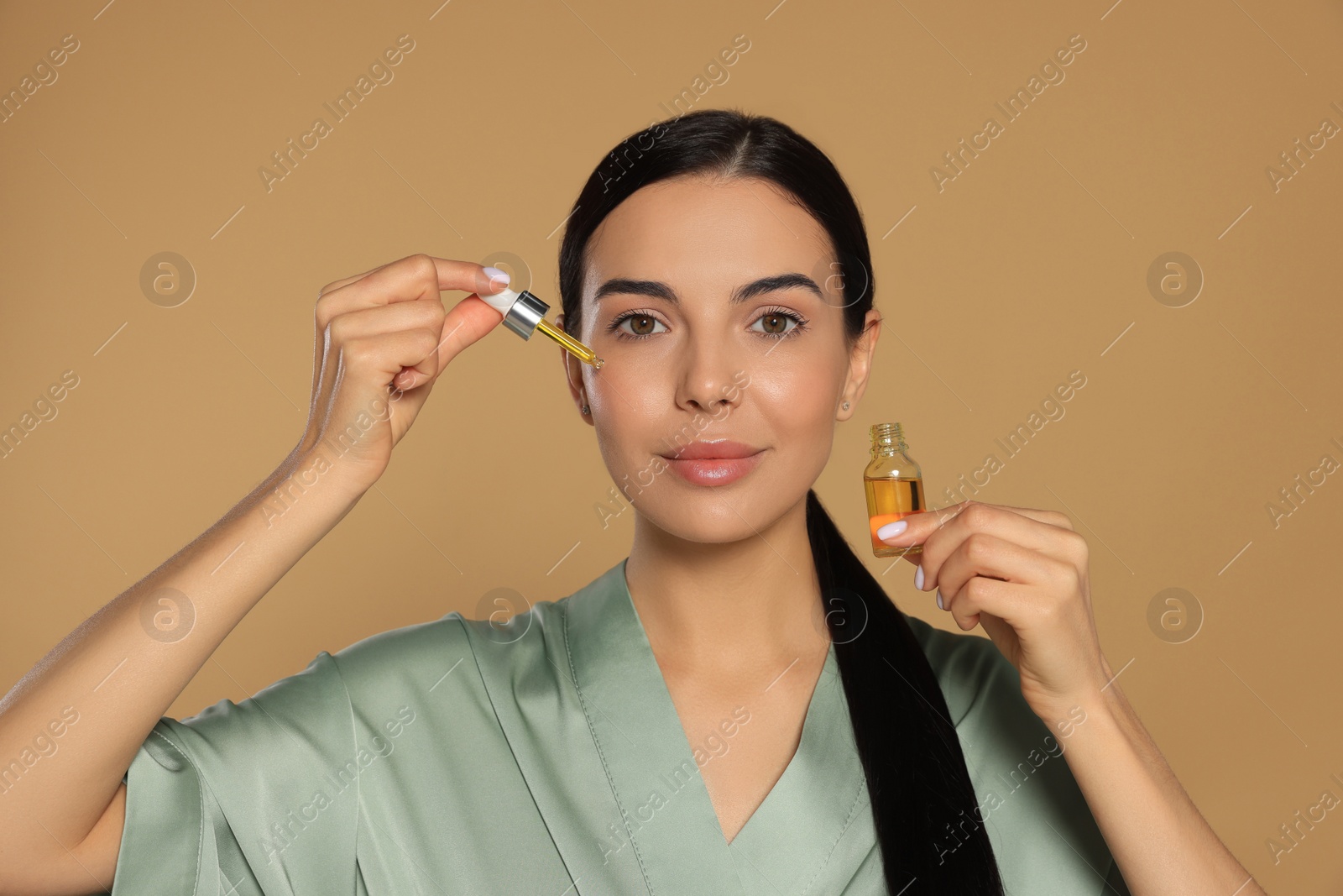 Photo of Young woman applying essential oil onto face against beige background