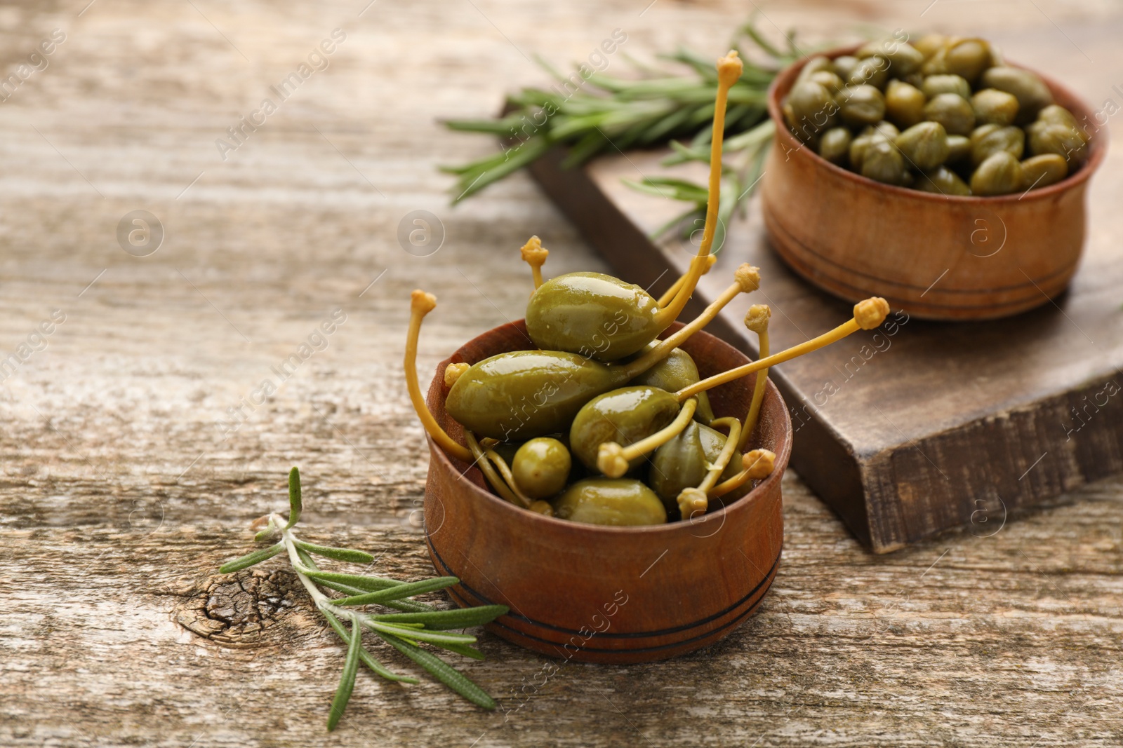 Photo of Delicious pickled capers and rosemary twigs on wooden table, closeup