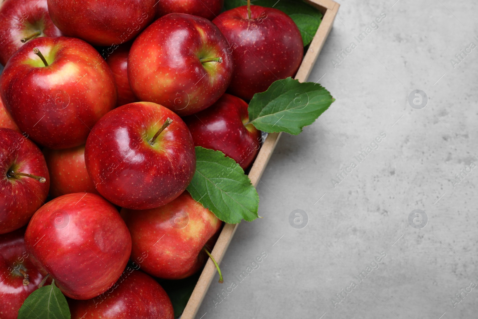 Photo of Juicy red apples in wooden tray on grey table, top view