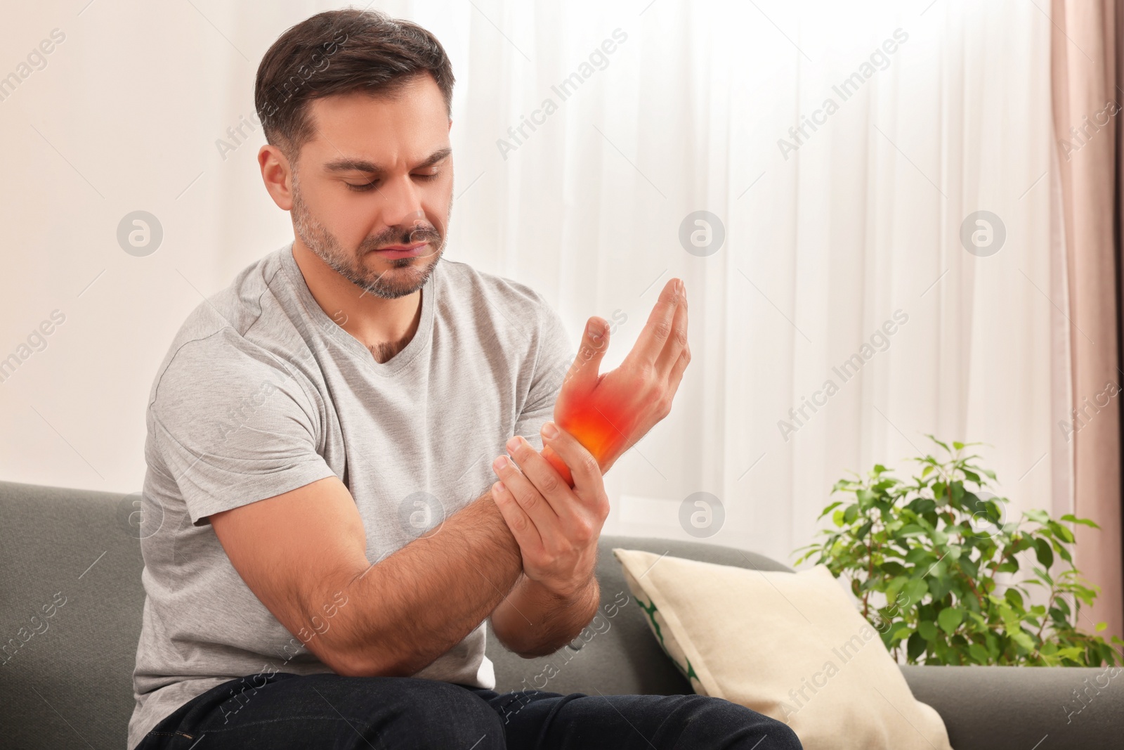 Image of Arthritis symptoms. Man suffering from pain in his hand on sofa at home