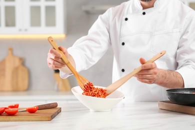 Photo of Professional chef putting delicious spaghetti into bowl at marble table in kitchen, closeup